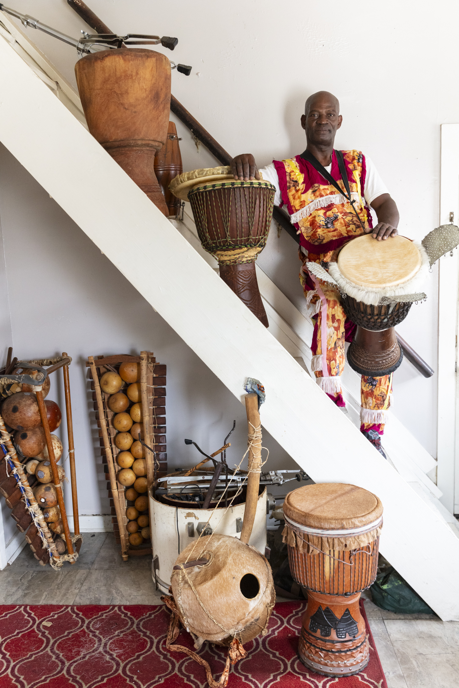 Koné stands with a collection of his handmade percussion instruments. He holds two rope-tuned djembe drums. Photo by Cedric Angeles.