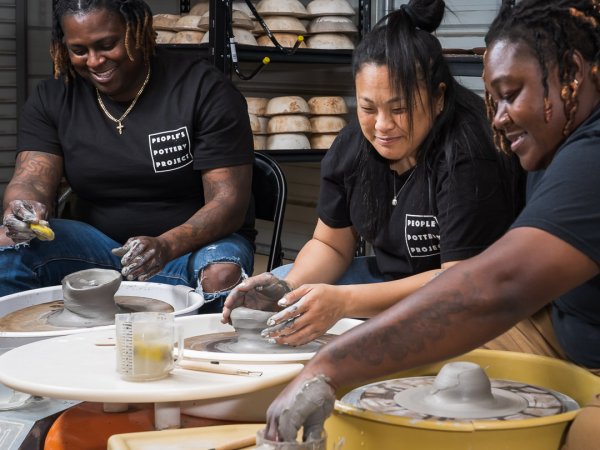 A group of people in matching black tshirts laughing and smiling while shaping pottery on wheels
