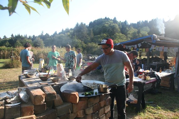 outdoor gathering of people around a kiln where food is being prepared on a griddle top and served