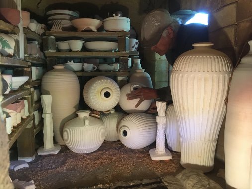 person crouching into a ceramics kiln to adjust the unfired pieces inside