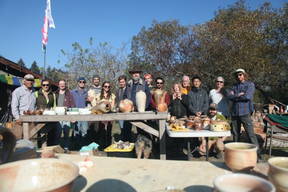 group of people posing for a photo beside tables of ceramic ware in an outdoor environment