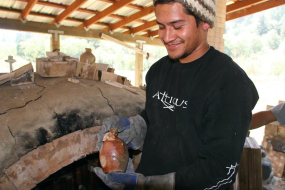 ceramic artist admiring small vessel pulled from wood fire kiln