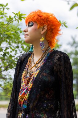 singer with orange hair and bold makeup wearing colorful jewelry and shirt and black cardigan