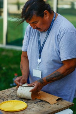 artist in blue shirt working on a craft project with a role of birch bark