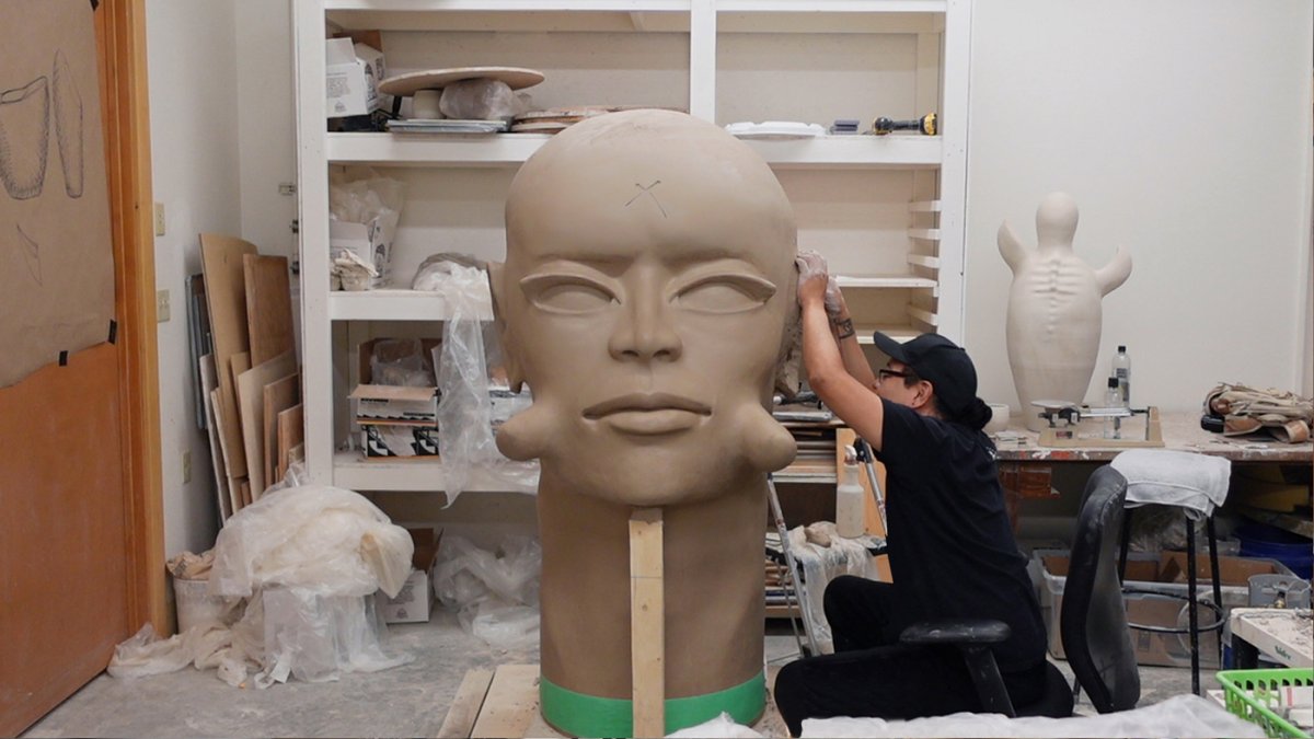 Ceramic artist working in studio on a large sculpture of a head