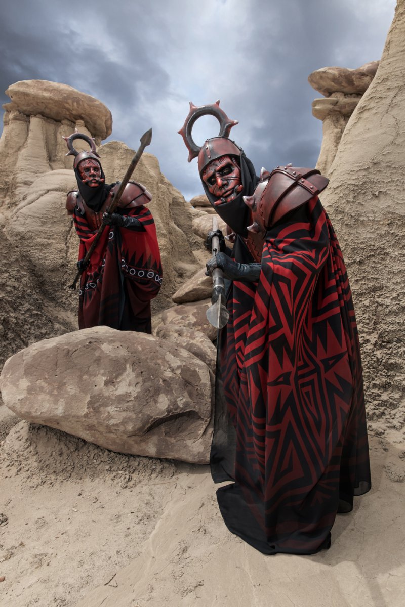 Figures wearing ornate masked costumes in a desert setting
