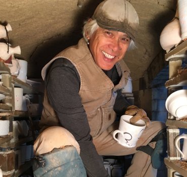 ceramicist conrad calimpong crouching in wood-fired kiln