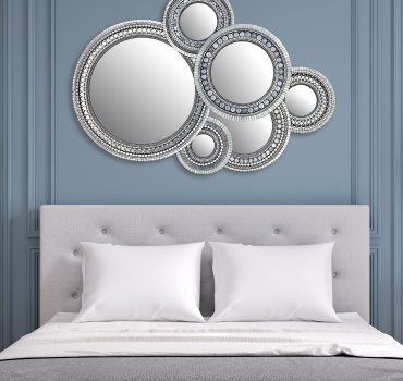 collage of overlapping round mirrors of different sizes with ornate mosaic frames pictured on a blue wall above a bed