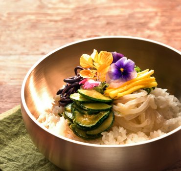 bronze korean yugi bowl filled with rice and vegetables and garnished with a flower