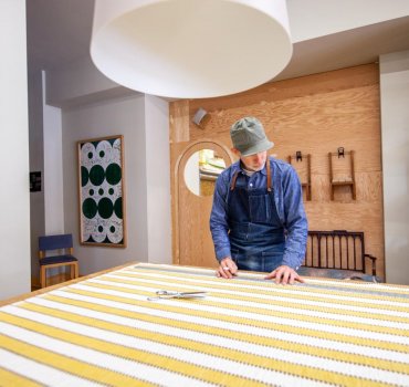 Upholstery artist measuring yellow striped fabric on a table in a studio
