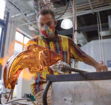 glass artist working in studio with goggles and a mask