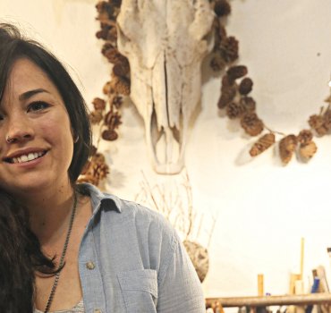 portrait of woman leaning out of frame with cow skull visible on wall in background