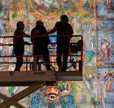 silhouette photo of three people on an elevated platform observing a colorful floor to ceiling artwork