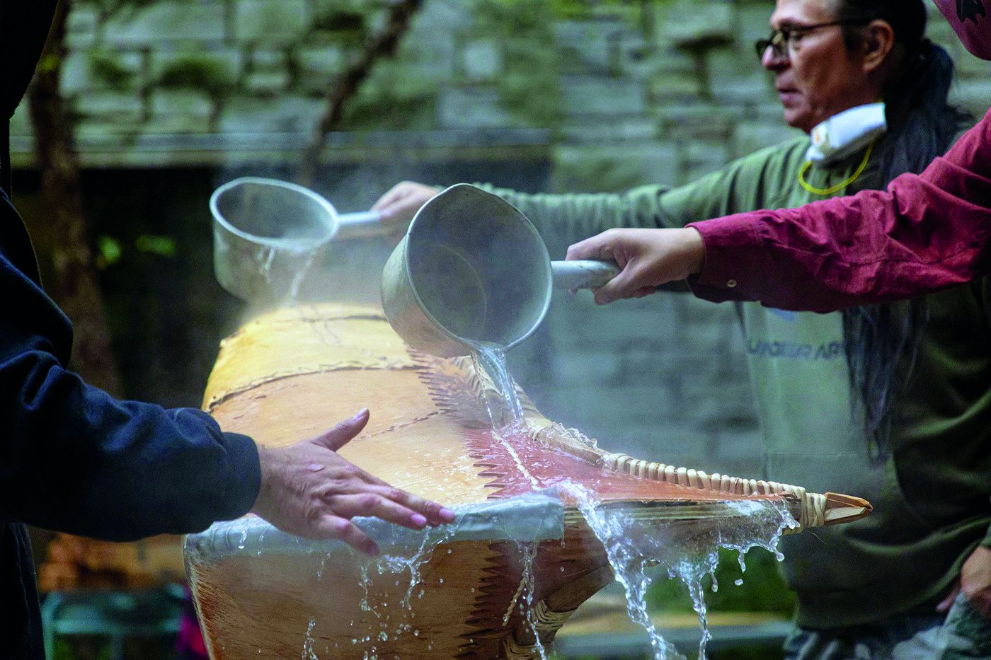 Group of people pours hot water to soften the wood used for constructing the canoe.