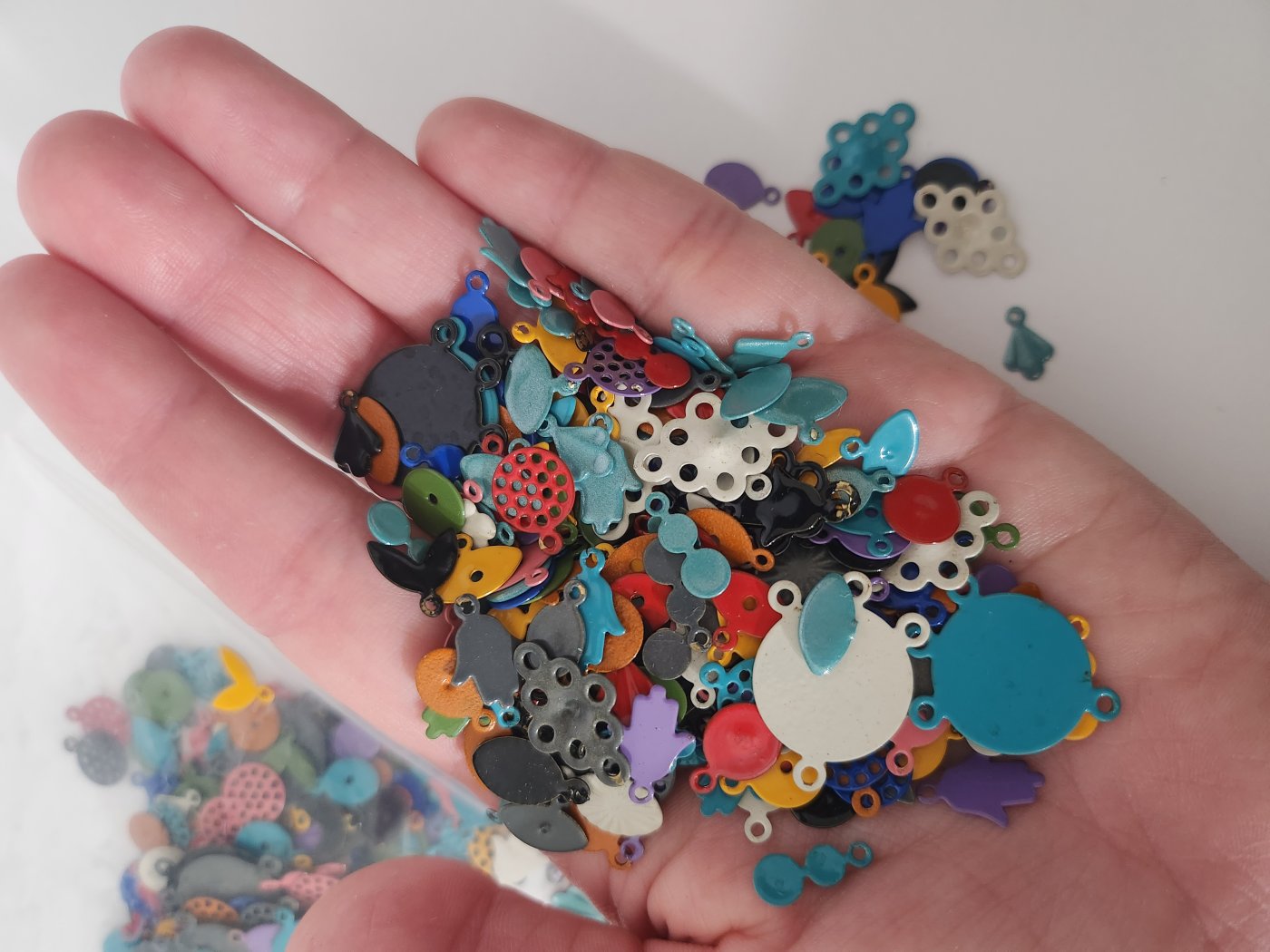 A hand holding multi-colored powder-coated metal charms. 