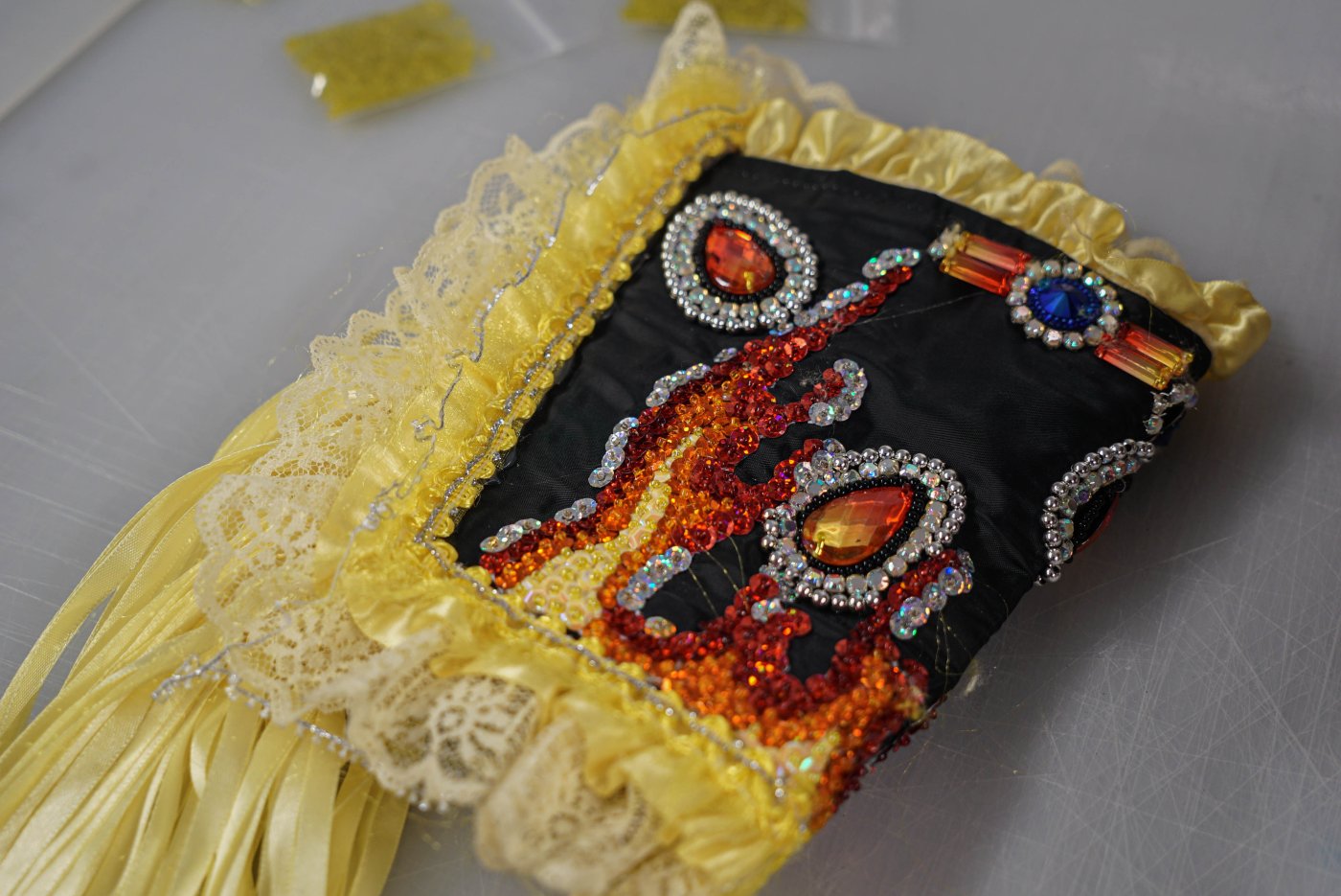 Close-up image of a beaded cuff with yellow fabric and orange, red, blue and blacks beads and stones.