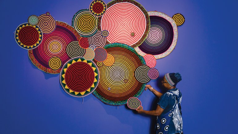 Person hanging colorful crocheted mandala art on a blue wall