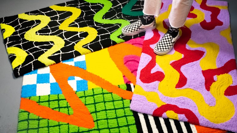 three colorful tufted rugs overlapping one another on a gray floor with a person wearing checkered slip on shoes and white pants standing on them