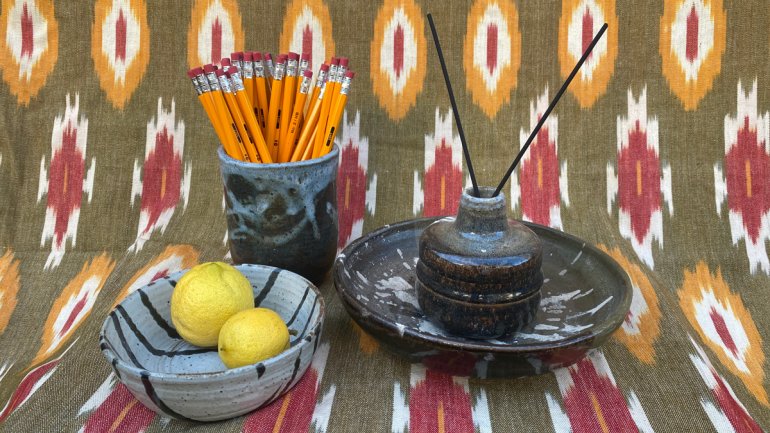 handmade ceramic vessels of different shapes holding lemons incense and pencils arranged against a patterned textile backdrop