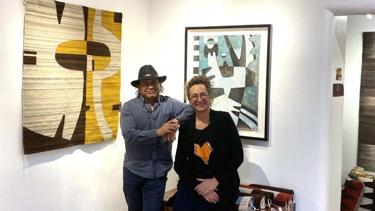 two artists posing in their studio with weavings and symbolist paintings hanging on the walls
