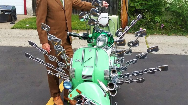 Portrait of kent aldrich wearing mask hat sunglasses and brown suit posing with decked out moped