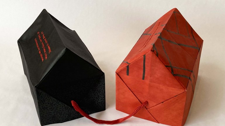 Paper sculpture of two houses one red and one black connected by a red string