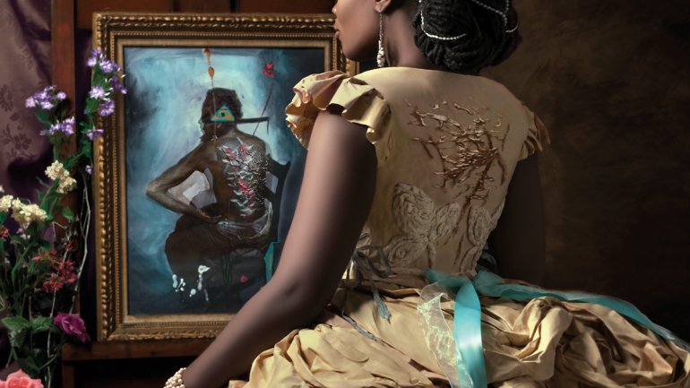 model wearing an ornte gold paper dress standing before a surrealist painting depicting a man seated on a chair