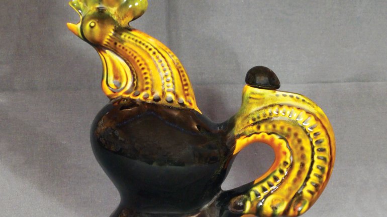 ceramic jug in the shape of a rooster with yellow head and tail and black body