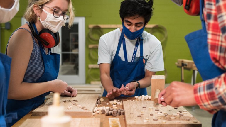 group of students wearing masks working on a wood projects aroumnd a table in a workshop