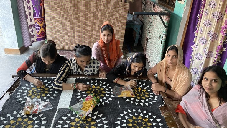 group of artists sitting around a table in india working on a series of black white and yellow patterned textiles