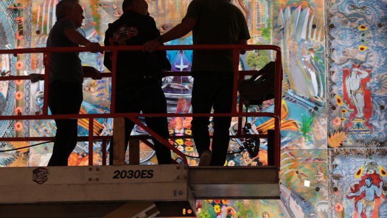 silhouetted photo of three people on an elevated platform observing a huge illuminated colorful artwork