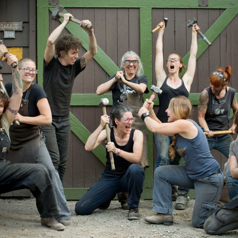 group of blacksmiths striking funny poses with hammers and other tools in front of a brown and green barn door