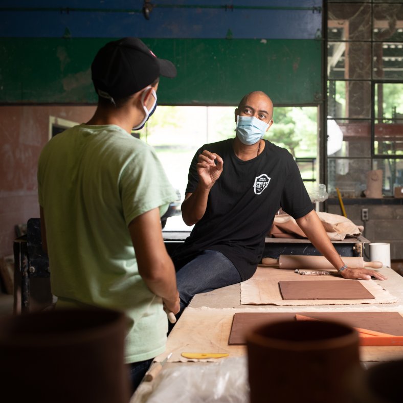 teacher wearing a mask providing instruction to two students in a workshop