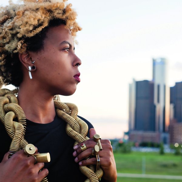 portrait of tiff massey with coiled gold necklace and large gold rings with detroit buildings in back on a summer evening