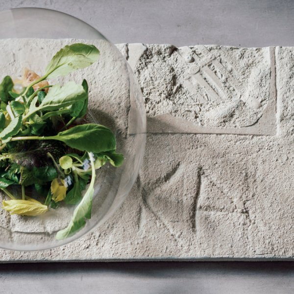 salad inside of a glass orb on a cement platter with carved letters and impressions