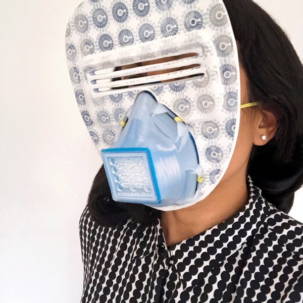 woman in black and white patterned blouse holding an face mask thats part decorative and part protective