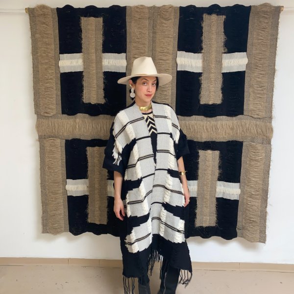 textile artist rhiannon griego posing in front of tan and black handwoven textile artwork