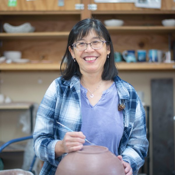 portait of ceramic artist standing studio smiling and preparing to etch into the bottom of a clay bowl