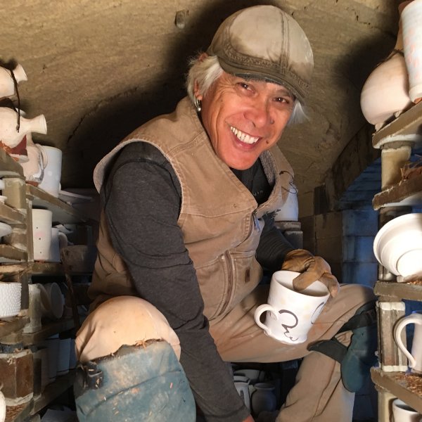 portrait of ceramist conrad calimpong crouched inside a kiln with unfired ceramics