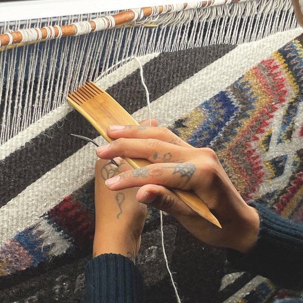 Two hands using a weaving comb.