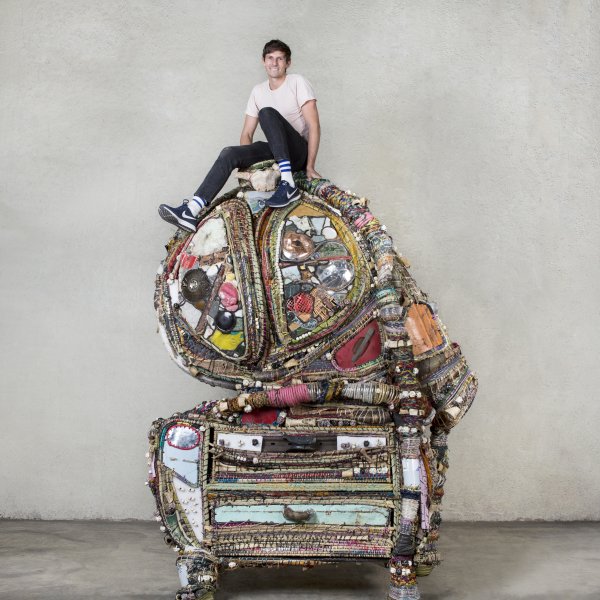 Misha Kahn seated on top of his sculpture Scrappy Grand, 2017, found objects, mixed media, ceramic beads, grass, fibers, 110 x 84.5 x 44.5 in. Photo by Daniel Kukla, courtesy of Friedman Bend and Misha Kahn.