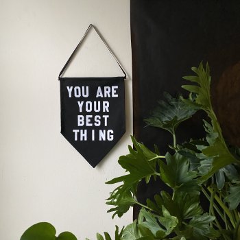 Black pennant with white lettering hanging on wall beside plant