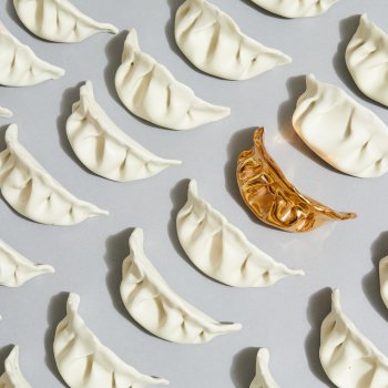Array of porcelain dumplings with one golden one on a gray surface