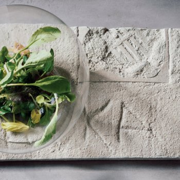 salad inside of a glass orb on a cement platter with carved letters and impressions