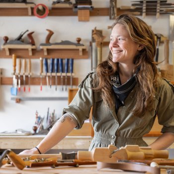 woodworker in studio looking away from camera and smiling while standing at bench with tools