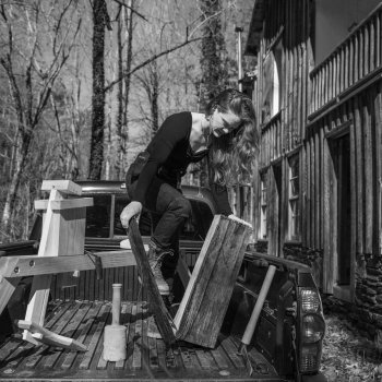 grayscale photo of a woodworker splitting a log in the back of a truck