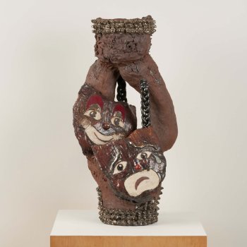 sculptural ceramic vessel featuring textured brown clay smiling and frowning masks and punk-inspired studs and chains