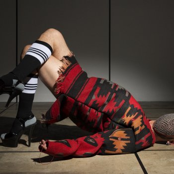 masked person in red orange and black smock with tall black and white stockings and high heels posed on the floor