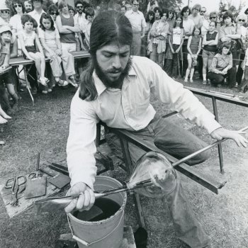 black and white photo of a glass blowing artist demonstrating technique at an outdoor craft fair