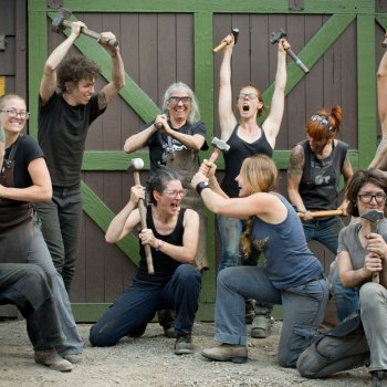 group of blacksmiths striking funny poses with hammers and other tools in front of a brown and green barn door
